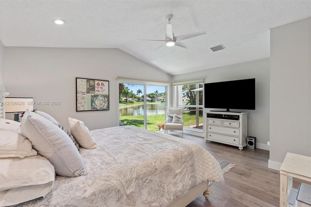 Vaulted ceiling with integrated lighting, wood-finish flooring, and expansive sliding glass doors opening to a water feature
