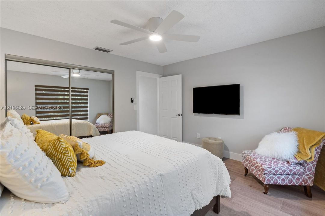 Neutral interior walls, wood-finish flooring, sliding mirrored closet doors, and a ceiling-mounted light fixture with fan