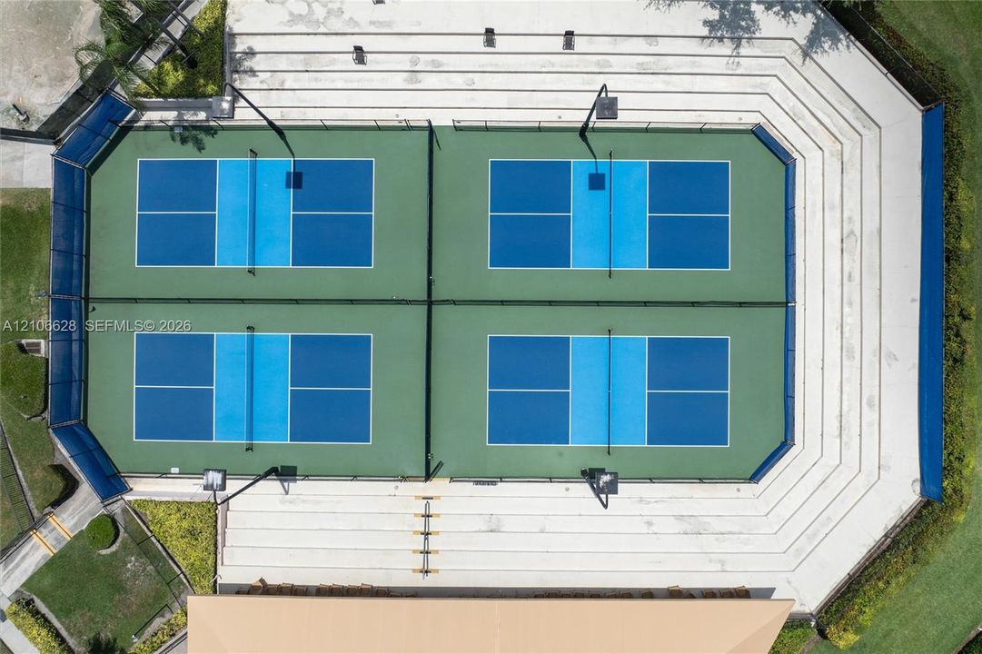 Four pickleball courts with perimeter fencing, integrated lighting, and terraced concrete spectator seating