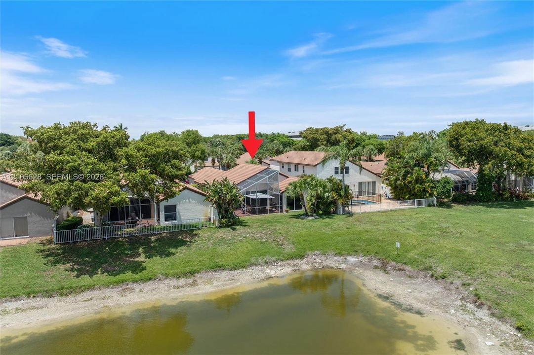 Aerial perspective of a multi-family property featuring a screened-in lanai, tile roof, pond frontage, and mature landscaping
