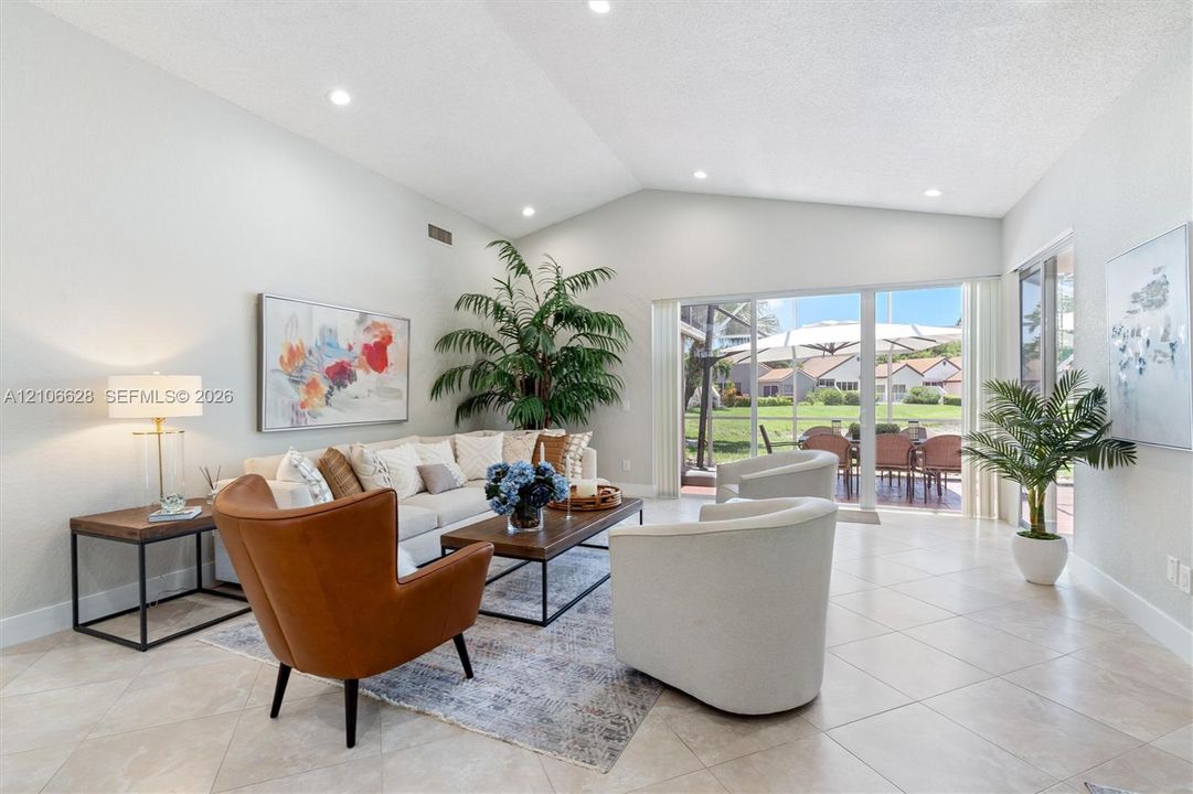 Vaulted ceilings, neutral ceramic tile flooring, recessed lighting, and large sliding glass doors providing access to a screened patio