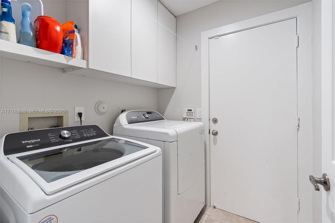 Laundry area featuring white flat-panel upper cabinetry, an open built-in shelf, and a solid-core door with satin nickel hardware