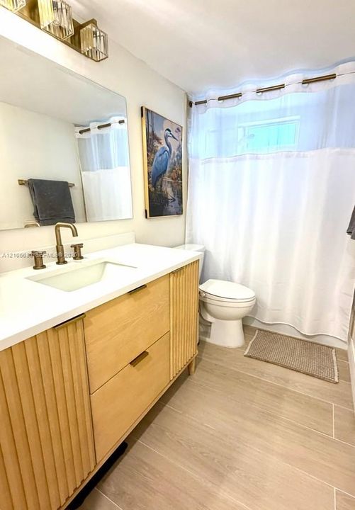 Custom wood-finish vanity with fluted detailing, quartz countertop, integrated rectangular sink, brass-tone hardware, and matching multi-light wall sconce
