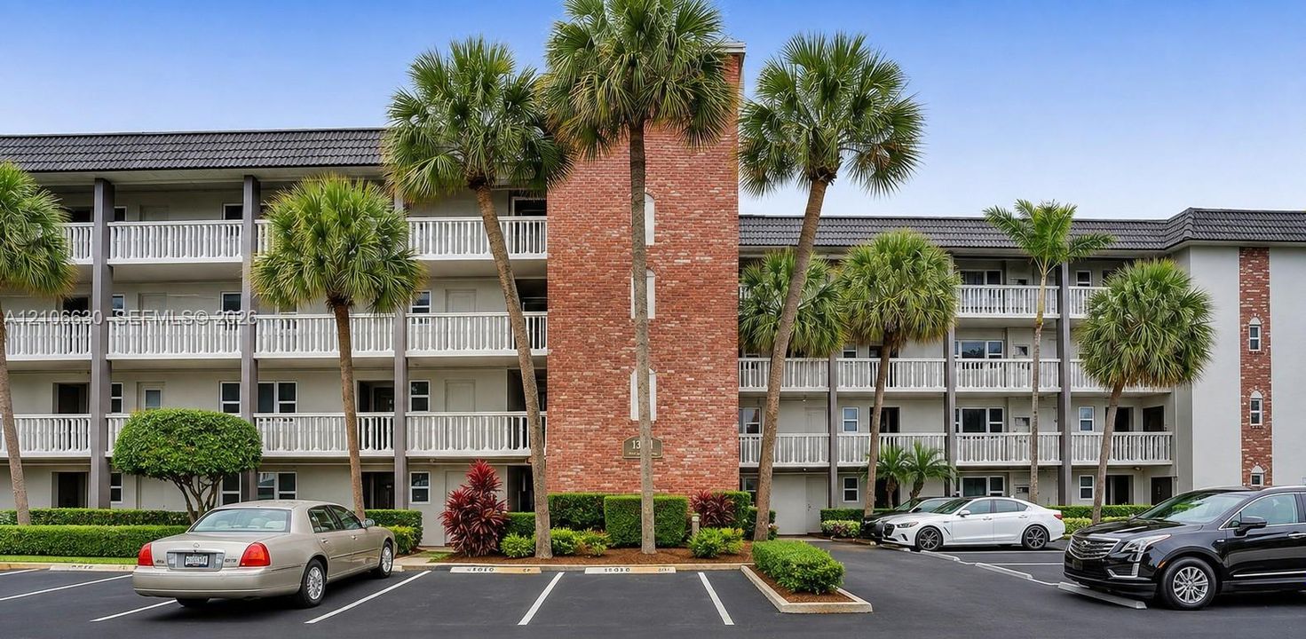 Multi-level exterior featuring a brick facade, white balcony railings, a dark shingled roof, and paved surface parking