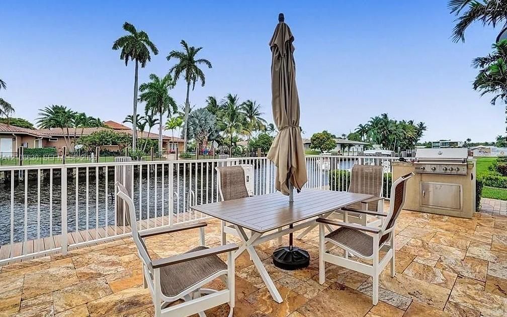 Waterfront patio featuring stone paver flooring, built-in outdoor grill, and white metal fencing