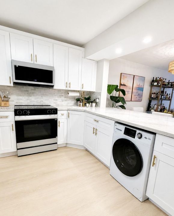Kitchen featuring white Shaker-style cabinetry, gold-tone hardware, a stone-patterned tile backsplash, solid-surface countertops, and built-in stainless steel appliances