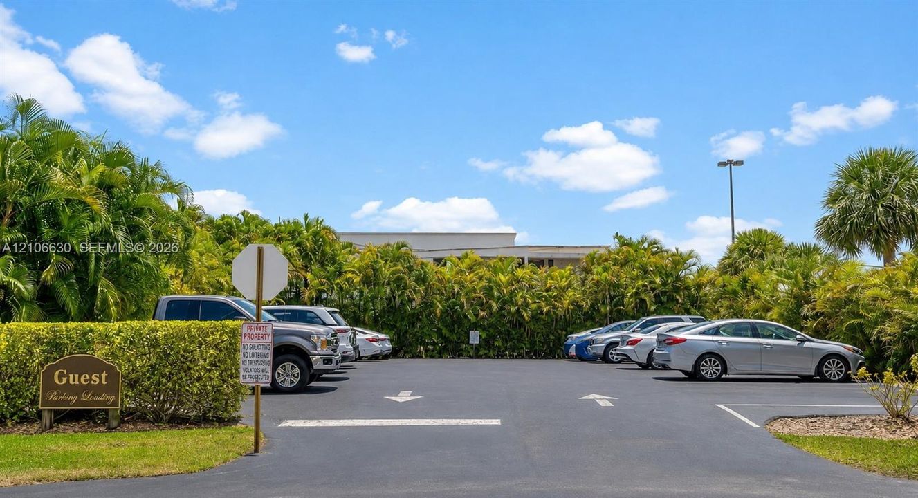 Dedicated guest parking area featuring paved asphalt surfaces, marked parking stalls, directional signage, and mature perimeter landscaping