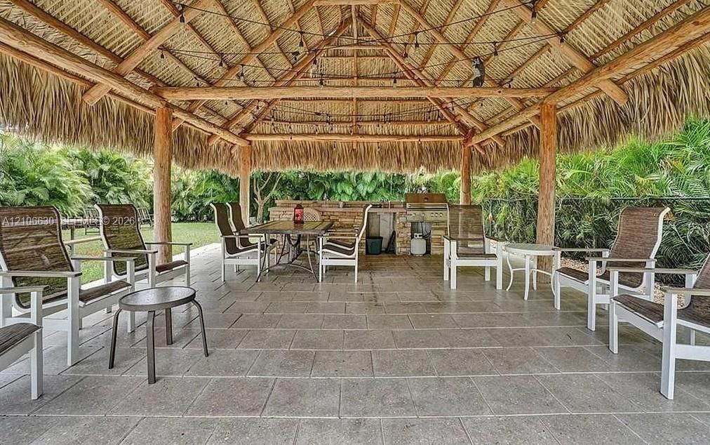 Outdoor pavilion featuring a thatched roof, exposed timber support beams, tiled flooring, and a stone-clad outdoor kitchen