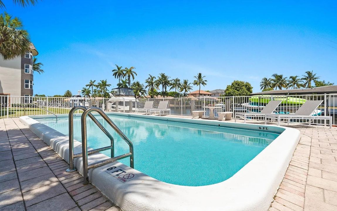 Swimming pool featuring a concrete deck, metal handrails, and a white perimeter fence
