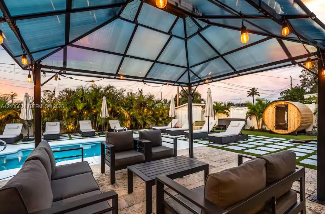 Outdoor living space featuring a dark-frame metal gazebo, private swimming pool, stone paver decking, synthetic turf accents, and a detached barrel sauna