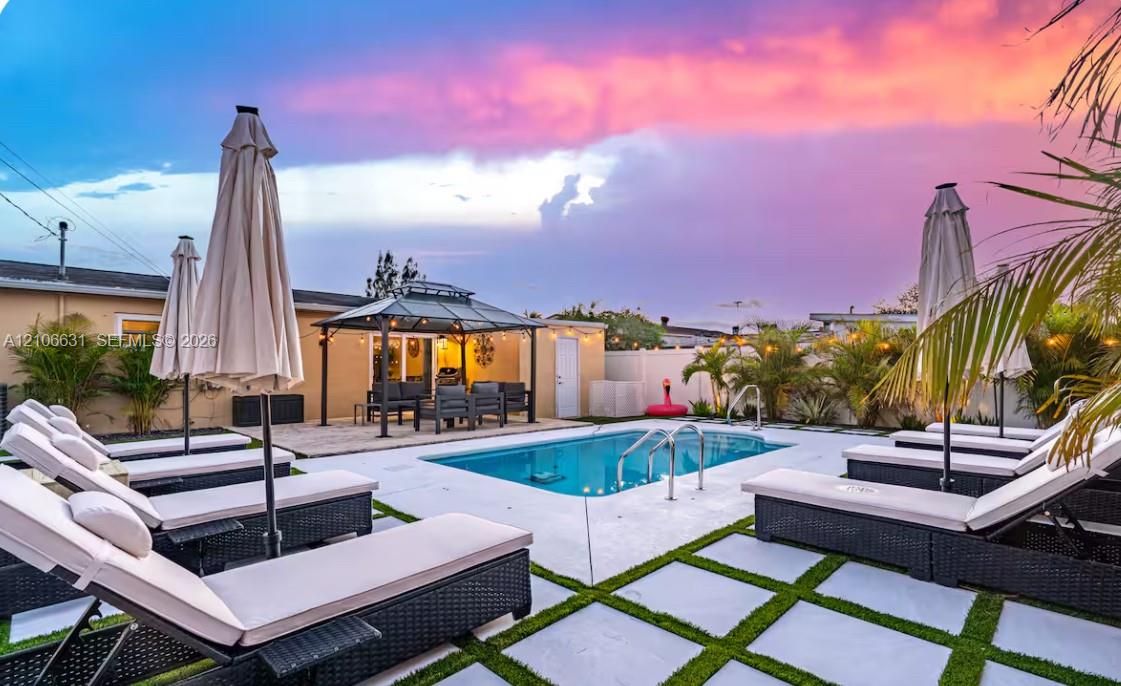 In-ground swimming pool with metal ladder, stone-paver pool deck, grass-grid inlay, and metal-frame gazebo