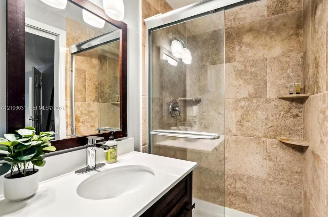 Bathroom featuring a stone-tiled shower with a glass enclosure, integrated corner shelving, vanity with a white countertop, and framed wall mirror