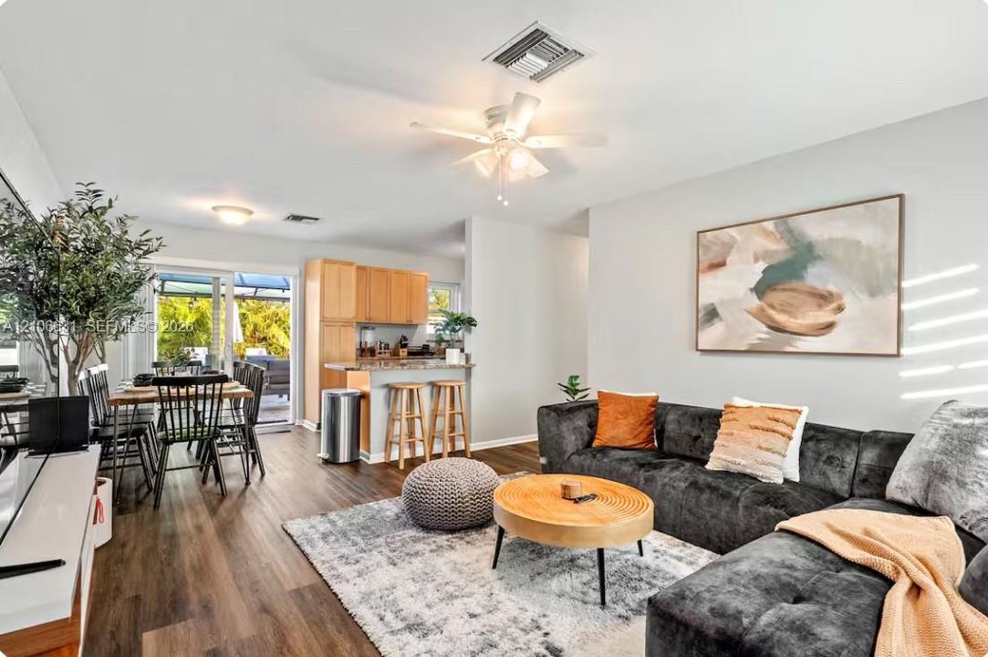 Open-concept interior featuring wood-finish flooring, a ceiling fan with integrated lighting, kitchen cabinetry with a breakfast bar, and a sliding glass door