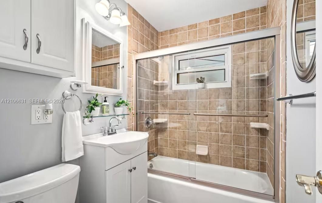 Bathroom featuring a white vanity cabinet with a integrated basin, sliding glass shower doors, tile-surround tub, framed wall mirror, and vanity lighting