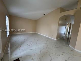 Interior room featuring vaulted ceilings, large-format tile flooring with a neutral veined pattern, and an arched architectural opening
