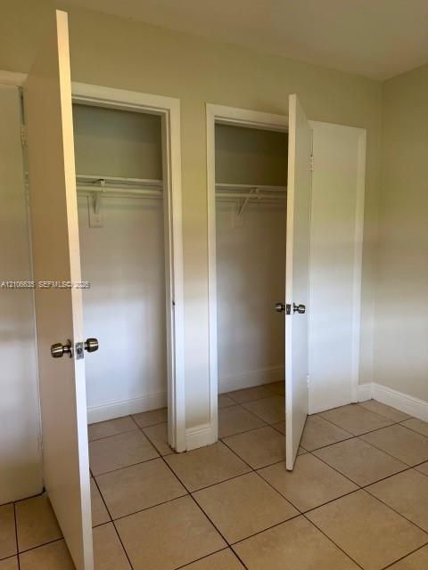 Dual closets featuring white swing doors, metal door hardware, and built-in shelving, complemented by ceramic tile flooring