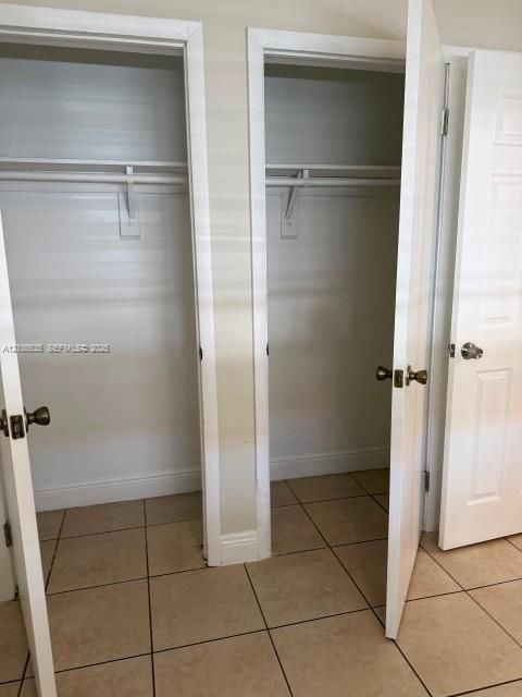 Dual reach-in closets featuring built-in hanging rods, upper shelving, and neutral-tone tile flooring