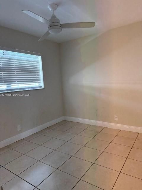 Neutral-toned room featuring large-format ceramic tile flooring, a white three-blade ceiling fan with integrated lighting, and a window fitted with horizontal blinds