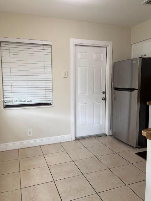 Ceramic tile flooring, stainless steel refrigerator, white six-panel door, and window with white horizontal blinds
