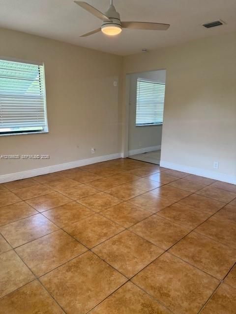 Neutral-toned interior featuring large-format ceramic tile flooring, a white ceiling fan with integrated lighting, and multiple windows fitted with horizontal blinds