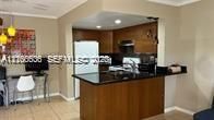 Kitchen featuring wood cabinetry, dark stone countertops, integrated breakfast bar, and recessed lighting