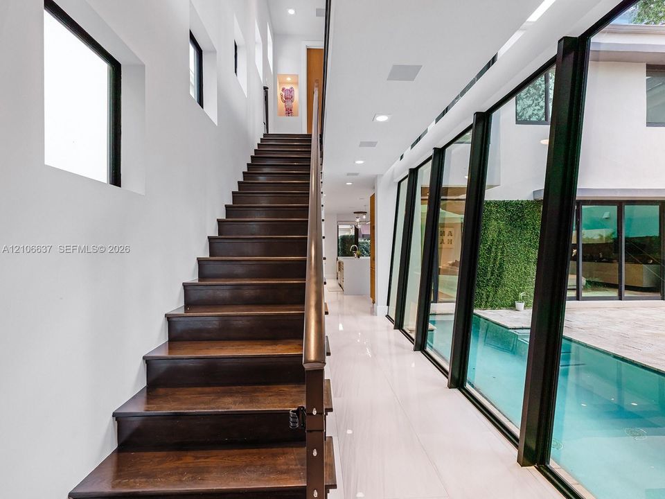 Staircase featuring dark wood treads and a linear handrail, large-format tile flooring, recessed ceiling lighting, and floor-to-ceiling glass wall panels overlooking a pool