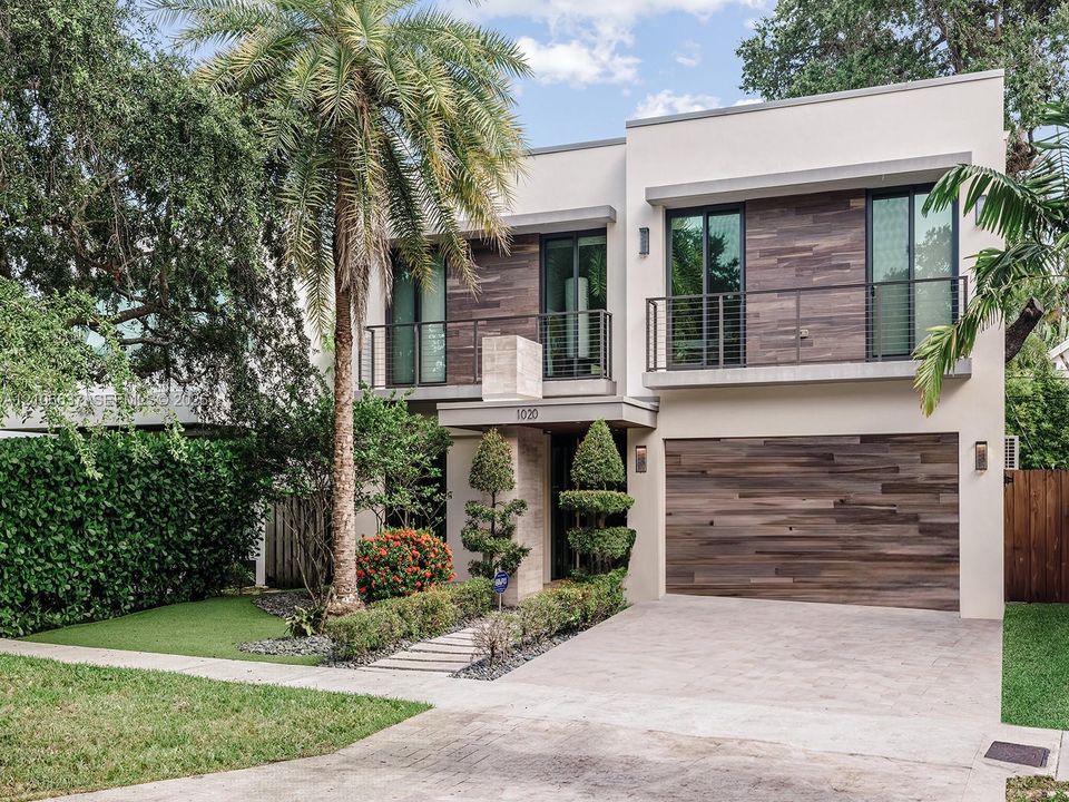 Modern two-story exterior featuring smooth stucco siding, horizontal wood-finish cladding, second-level balconies with metal railings, and an attached multi-car garage
