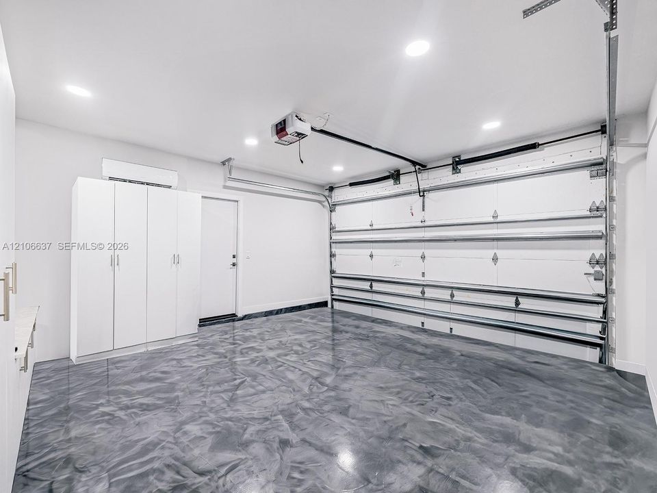 Garage featuring high-gloss epoxy flooring, built-in white cabinetry, recessed LED lighting, and a climate control unit