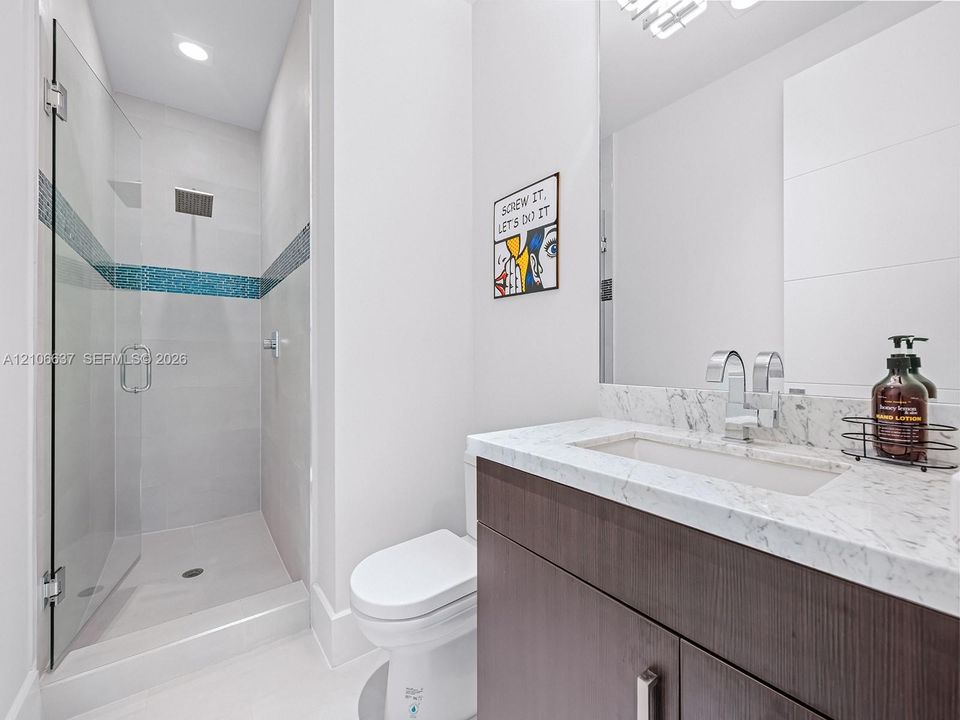 Modern bathroom featuring a dark wood-finish vanity, light-toned stone-finish countertop with an integrated rectangular sink, glass-enclosed shower with decorative tile inlay, and chrome fixtures