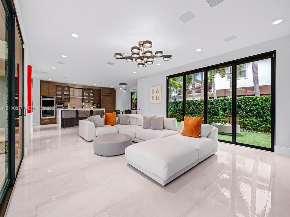 Open-concept living space featuring large-format tile flooring, multi-panel sliding glass doors, built-in cabinetry, recessed lighting, and a modern tiered chandelier