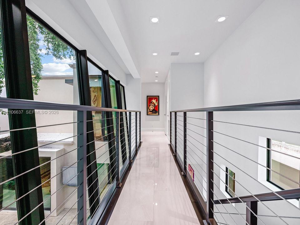 Hallway featuring polished light-toned flooring, recessed ceiling lighting, and a metal cable railing system with dark-finish posts, complemented by floor-to-ceiling glass paneling
