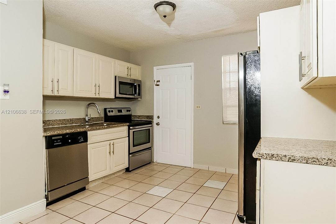 Kitchen featuring off-white cabinetry, stone-finish countertops, stainless steel appliances, and ceramic tile flooring