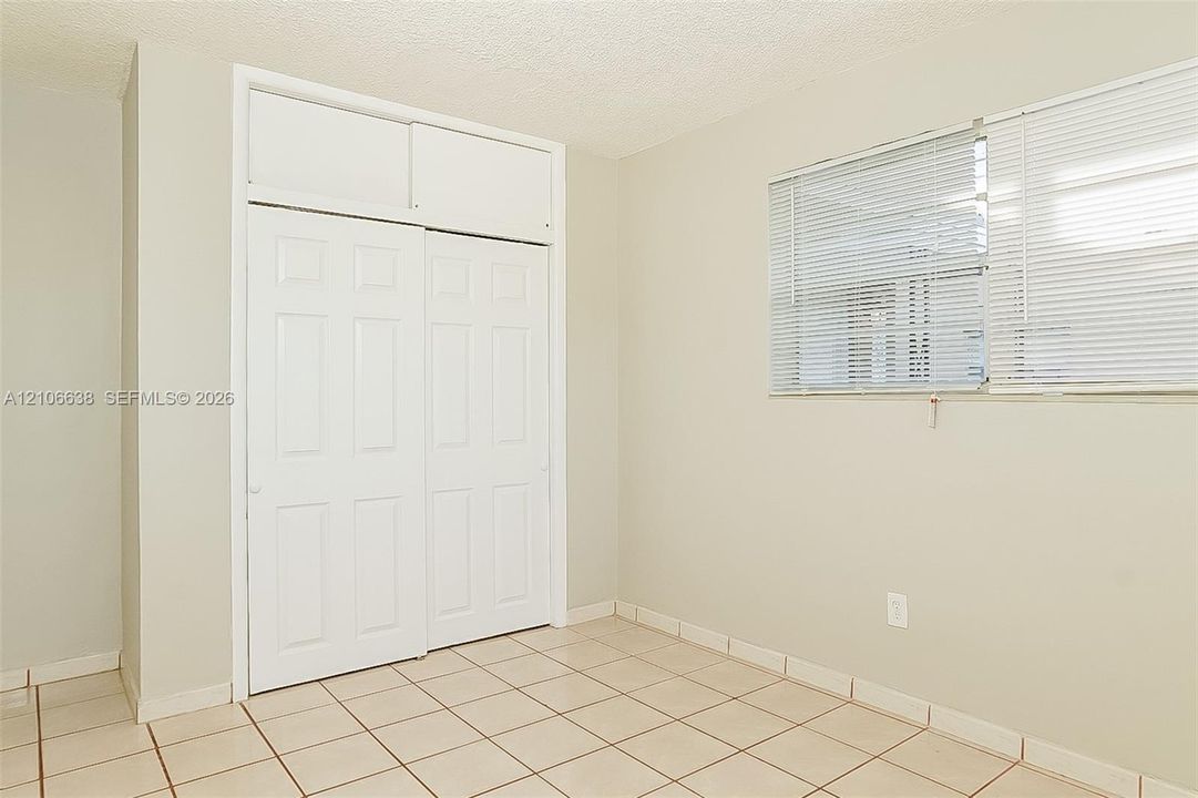 Room featuring tile flooring, neutral wall tones, and a built-in sliding closet with overhead storage compartments