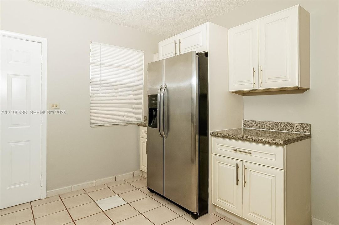 Kitchen featuring white shaker-style cabinetry, stone-finish countertops, stainless steel side-by-side refrigerator, and ceramic tile flooring