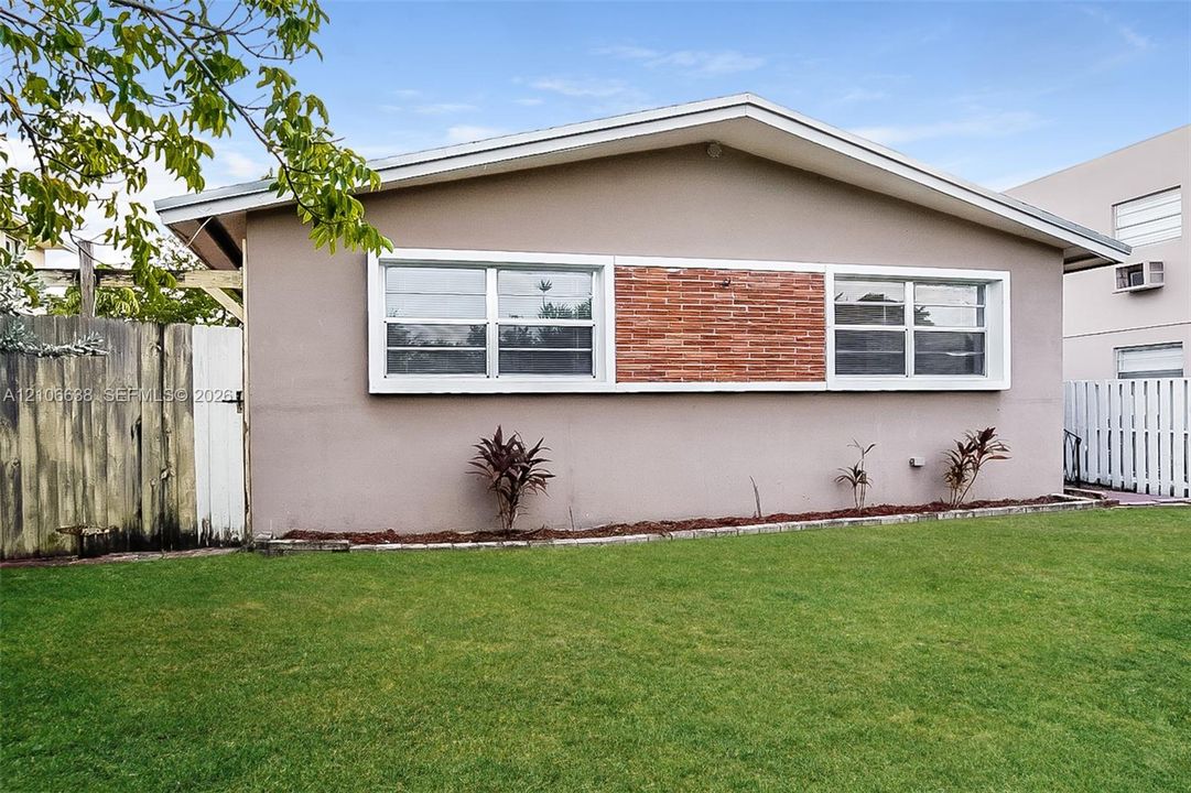 Exterior facade featuring stucco siding, central brick accent panel, expansive windows with white trim, and a low-pitched roofline set above a grass lawn
