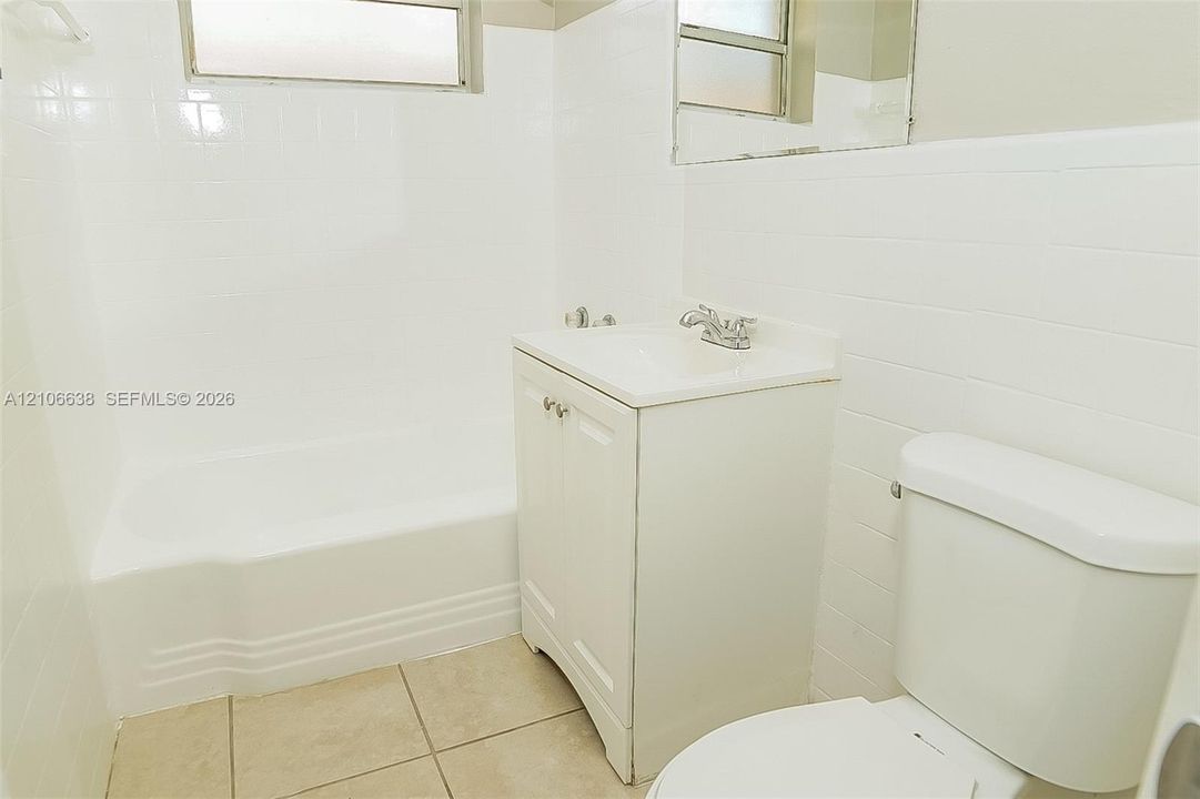 Bathroom featuring white tile surround, tub-shower combination, vanity with integrated basin, and neutral floor tile