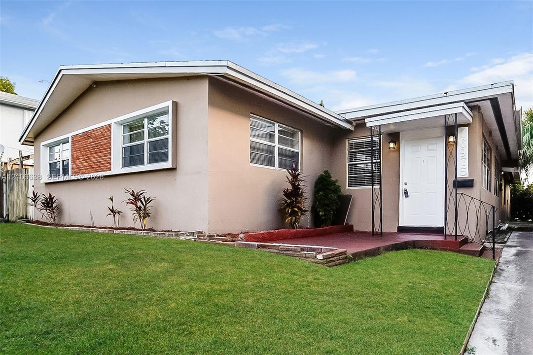 Mid-century inspired exterior featuring stucco siding, decorative brick accent detailing, a covered entryway with metal railing, and a gabled roofline