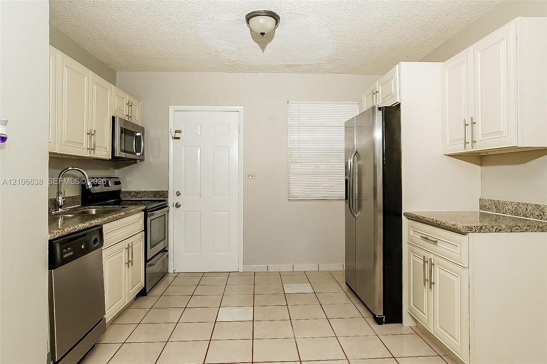 Kitchen featuring white cabinetry, stone-finish countertops, stainless steel appliances, and tiled flooring