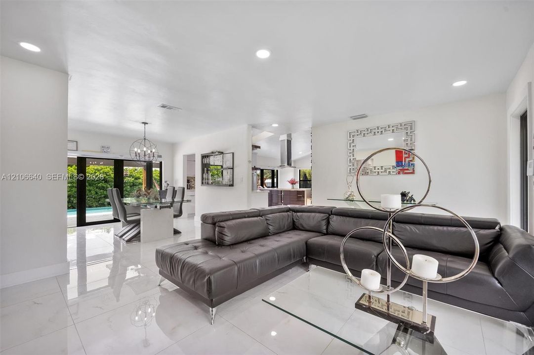 Recessed ceiling lighting, glossy white flooring, modern glass dining table, contemporary chandelier, and sliding glass doors