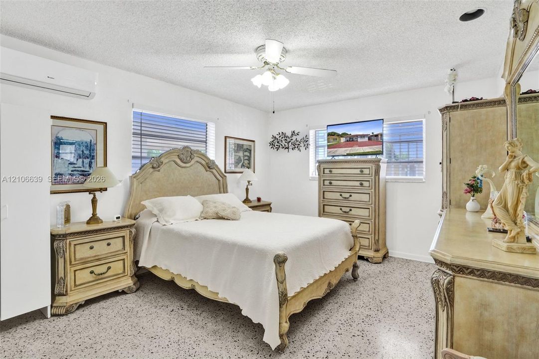 Interior space featuring white walls, terrazzo flooring, a multi-blade ceiling fan with integrated lighting, and a wall-mounted ductless air conditioning unit