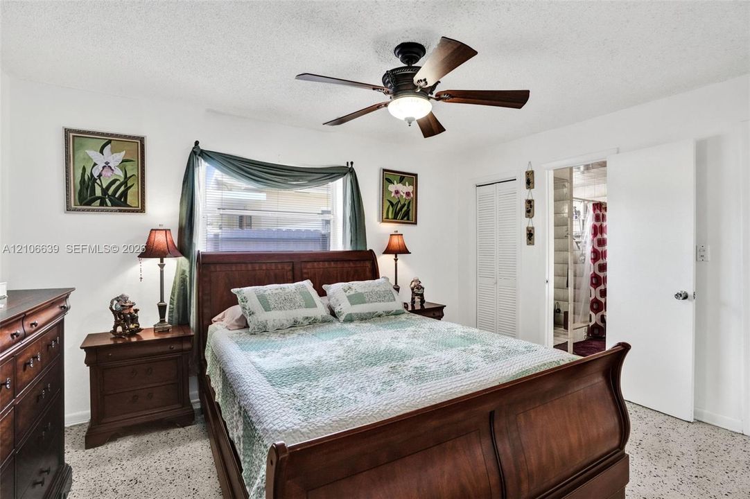 Bedroom featuring terrazzo flooring, white walls, louvered closet doors, and a ceiling fan with integrated lighting