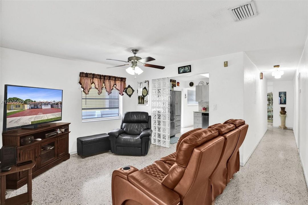 Living area featuring terrazzo flooring, a ceiling fan, and decorative glass block partition