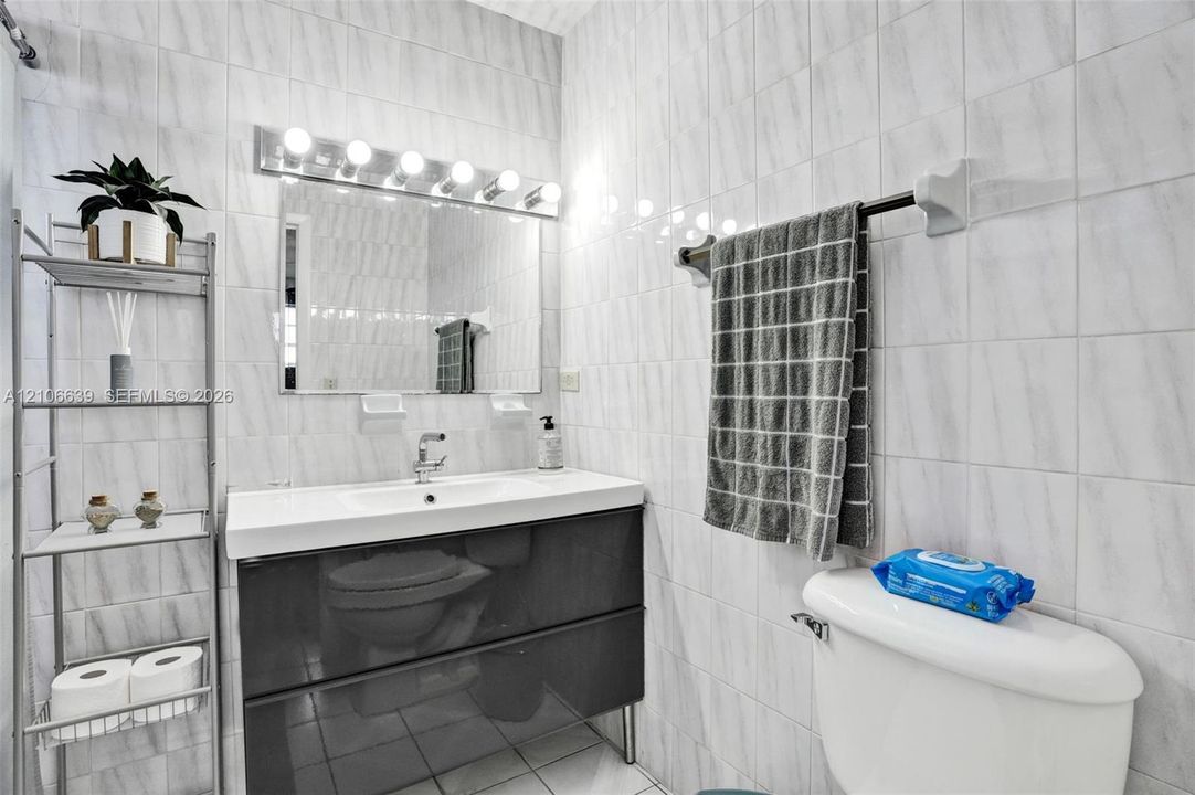 Wall-to-wall tiled surfaces, vanity with a rectangular basin, high-gloss cabinetry, and multi-bulb linear vanity lighting