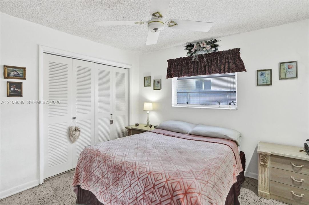 Bedroom featuring a ceiling fan with integrated lighting, dual louvered closet doors, and window with horizontal blinds