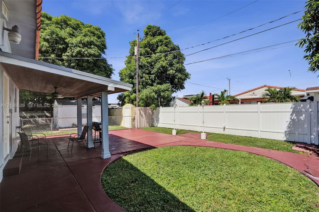 Covered patio featuring a wood-toned ceiling, white support columns, and red concrete hardscaping within a fenced backyard