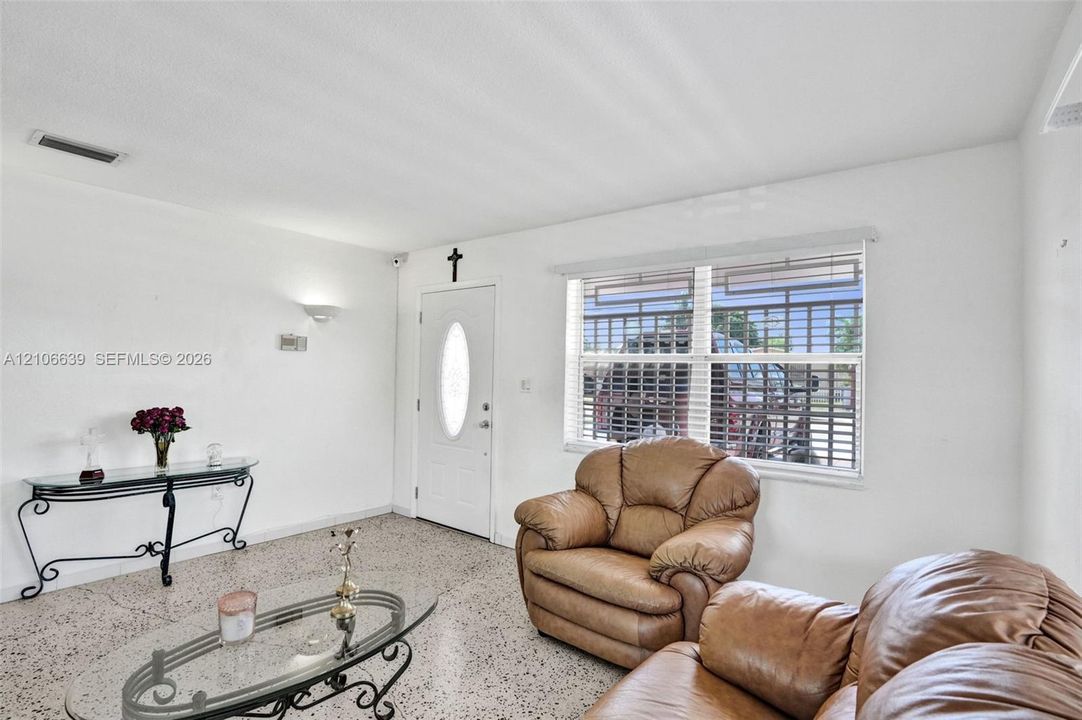 Living space featuring terrazzo flooring, white walls, and a recessed-panel entry door with an oval glass insert
