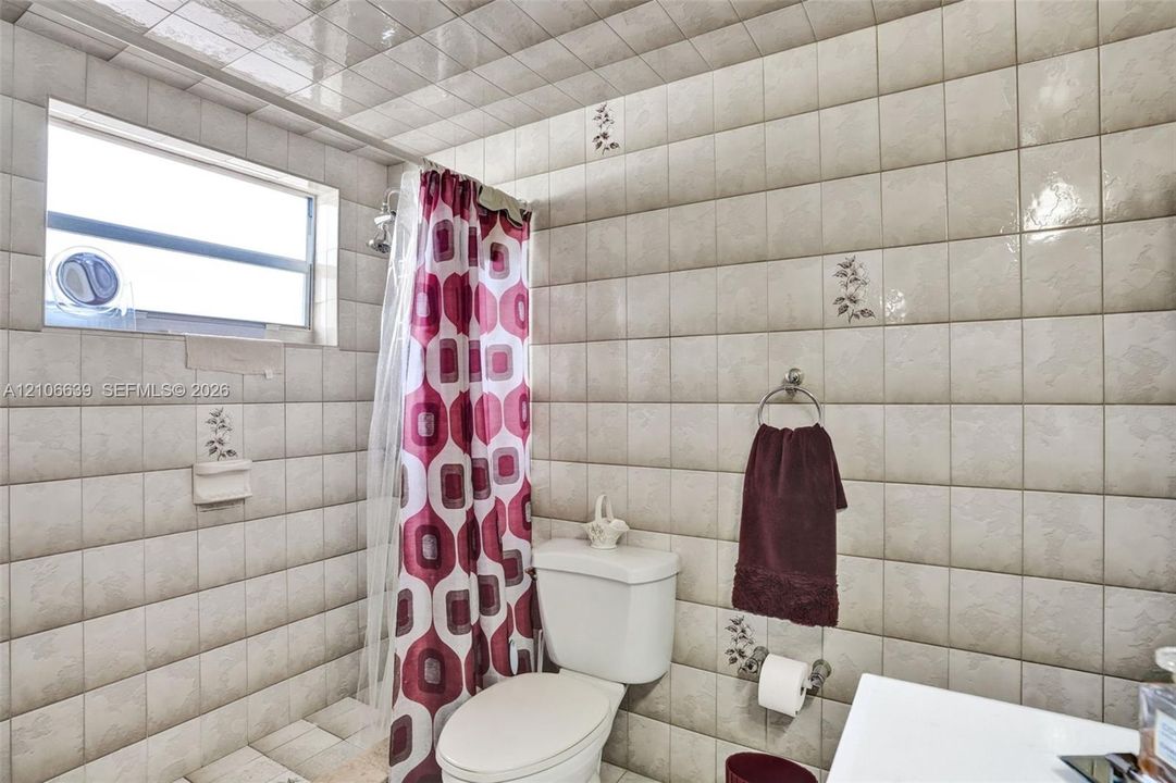 Full-height ceramic wall tiling, high-gloss ceiling tiles, integrated soap dish, and a horizontal window