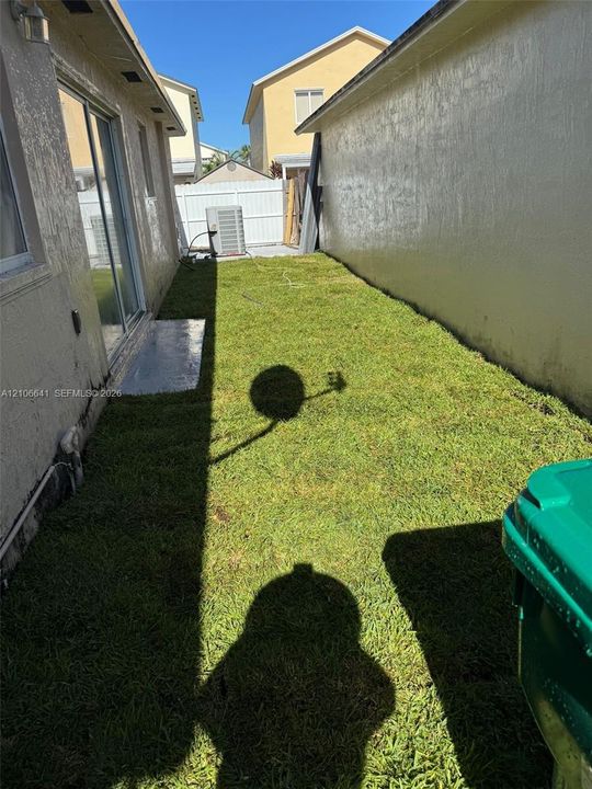 Side yard featuring a grass lawn, white vinyl perimeter fencing, and concrete patio entry