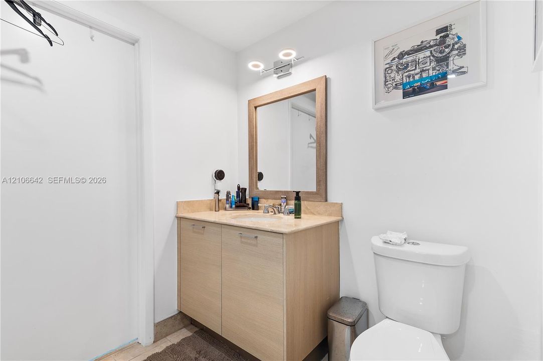 Vanity featuring wood-finish cabinetry, stone countertop with integrated sink, framed mirror, and dual-light fixture