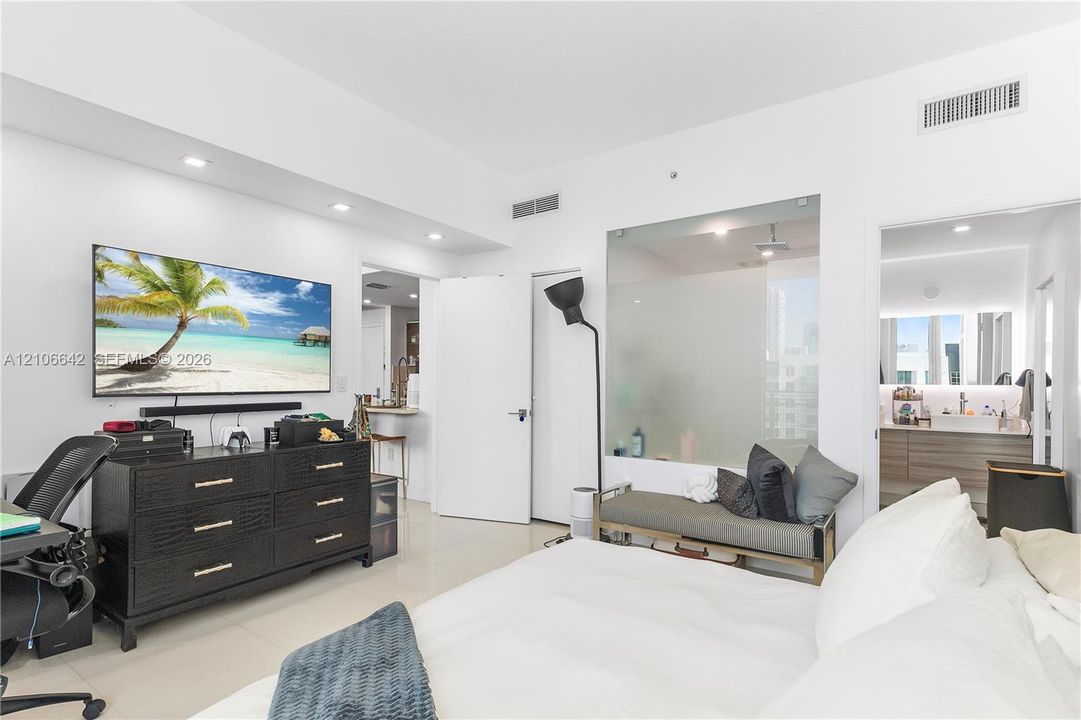 Interior room featuring light-toned flooring, recessed ceiling lighting, a floor-to-ceiling glass wall partition, and a doorway with a vanity visible